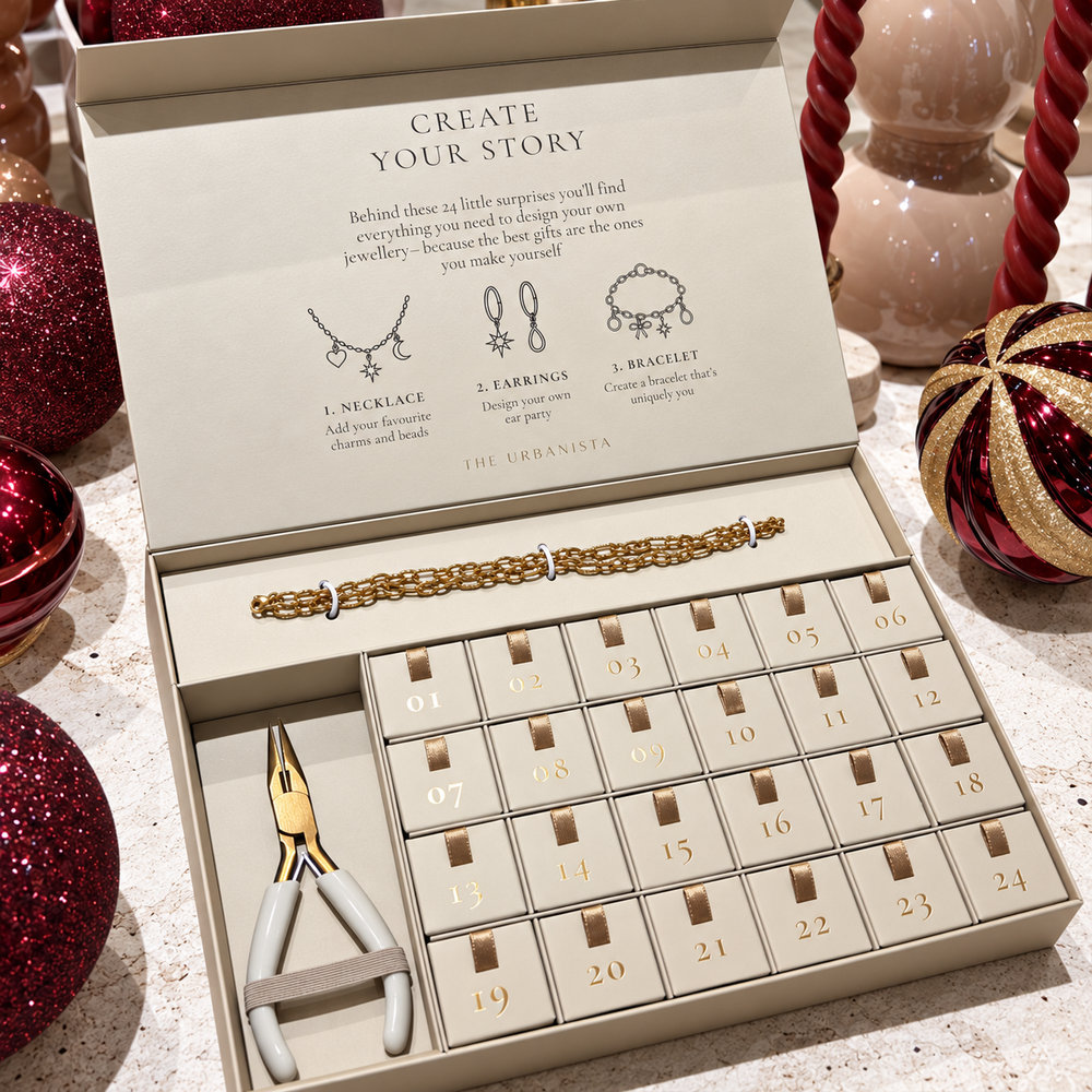Charm Bar Advent Calendar van The Urbanista met rode en beige verpakking, gouden bedels en de tekst 24 Little Surprises, Endless Ways to Create