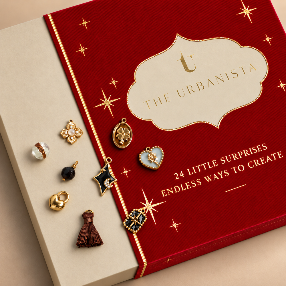 Charm Bar Advent Calendar van The Urbanista met rode en beige verpakking, gouden bedels en de tekst 24 Little Surprises, Endless Ways to Create